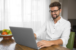man working remotely on laptop at kitchen table