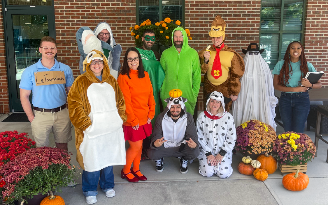 Eleven team members dressed in creative and festive Halloween costumes, posing together with smiles.
